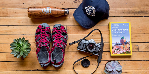 Un arrangement d’équipement comprenant une bouteille d’eau, une casquette, des sandales, une caméra et un guide de voyage.