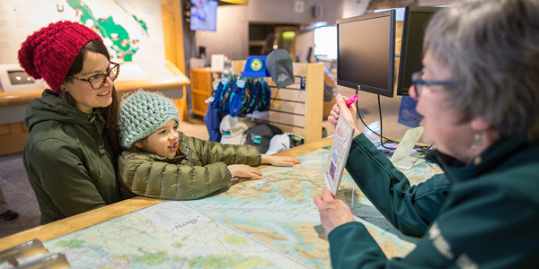 Une mère et sa fille étudient une carte avec une employée de Parcs Canada.