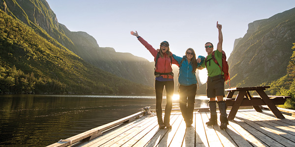 Three friends arms in air on dock in the back of Western Brook Pond, Gros Morne National Park
