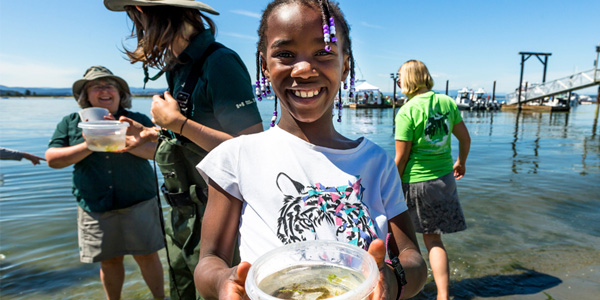 A young volunteer shows a fish caught during a species survey at the beach.