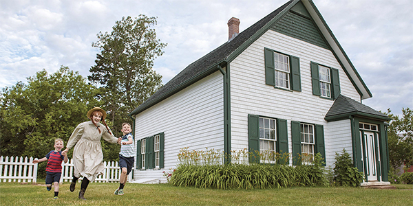 An interpreter dressed as Anne Shirley runs with children in front of Green Gables Heritage Place.