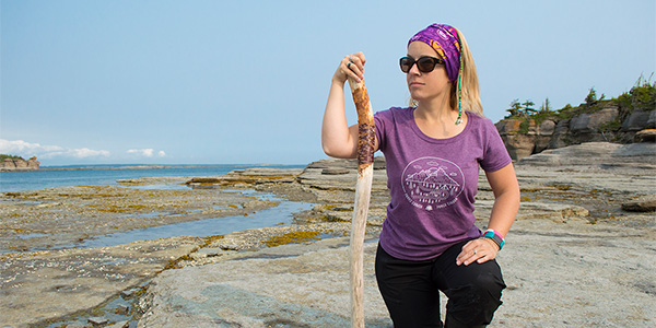 Une femme portant un t-shirt Né pour explorer et un Tuber’z zen sur la plage de la réserve de parc national de l’Archipel-de-Mingan.