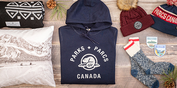 Les produits dérivés de Parcs Canada disposés de façon festive avec des cônes de pin décoratifs.