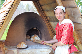 Une interprète en costume d’époque fait une démonstration de la cuisson traditionnelle du pain au four d’argile au lieu historique national du Fort-St. Joseph.