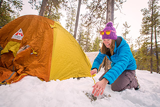 Une femme souriante s’installe pour faire du camping d’hiver dans le parc national Jasper.