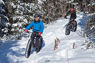 Two people enjoy fat biking at La Mauricie National Park on a sunny winter day.