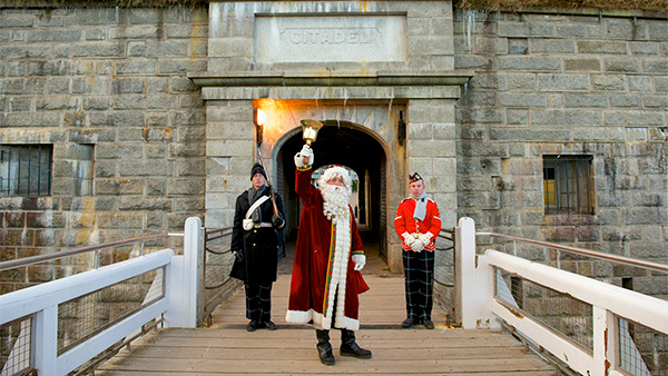 Father Christmas rings a bell as he stands at the entrance of the Halifax citadelle National Historic Site beside two Highlanders.