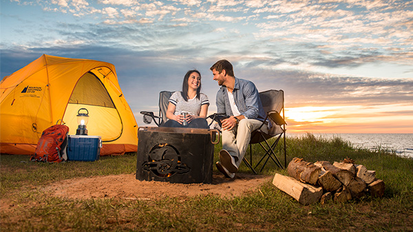 Un couple profite d’un feu de camp au coucher du soleil au terrain de camping de Cavendish au parc national de l’Île-du-Prince-Édouard.