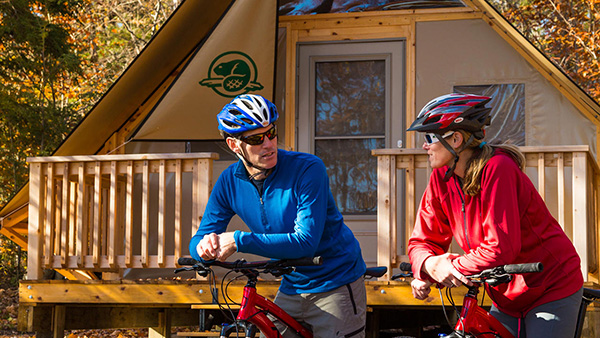 Un couple en vélo de montagne devant une oTENTik au terrain de camping de la Source aux Cèdres sur l’île Beausoleil dans le parc national des Îles-de-la-Baie-Georgienne.