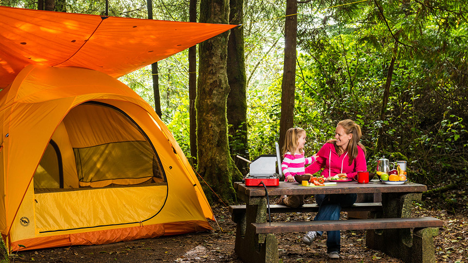 Une mère et sa fille prennent une collation à la table de pique-nique du camping à côté de leur tente.