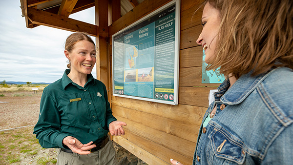 A young women chats with a Parks Canada staff member in front of a kiosk at Gulf Islands National Park Reserve.